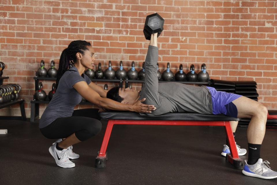 a personal trainer helping a client do a dumbbell bench